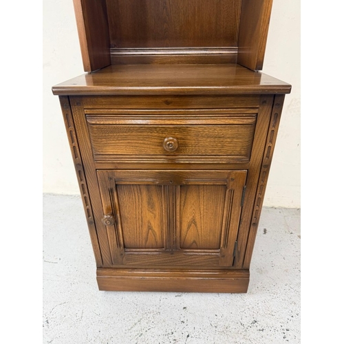 149 - A dark Ercol narrow bookcase or display cabinet, glazed and with a single drawer, single door unit u... 