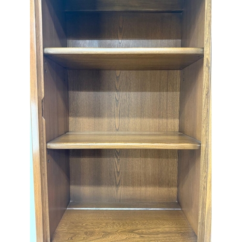 149 - A dark Ercol narrow bookcase or display cabinet, glazed and with a single drawer, single door unit u... 