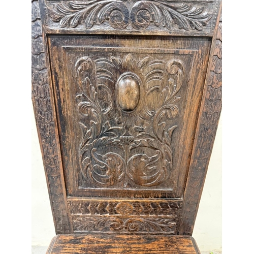 171 - An oak Jacobean-style hall chair with a heavily carved back ad on turned legs