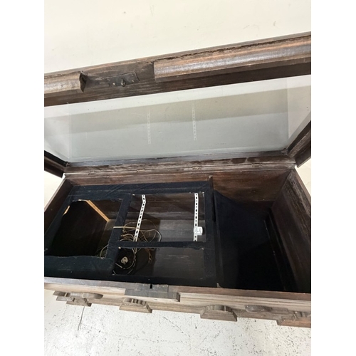 150 - A hardwood storage trunk with carved detail to the side and a glazed lid opening to a selection inte... 
