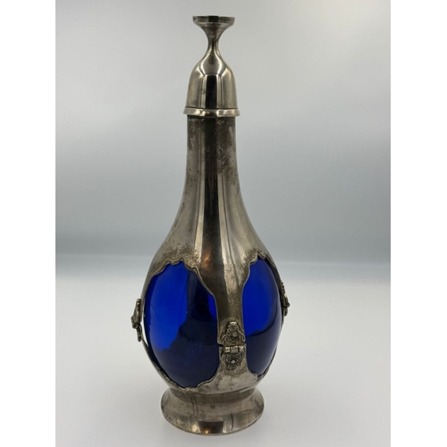 395 - An Art Nouveaux cobalt blue decanter encase in white metal with small glass screw top cup. Height ap... 
