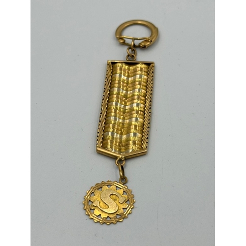 577 - An Arabian three colour gold key ring with an embossed S pendant.