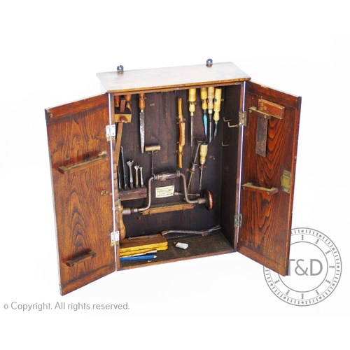 956 - An Edwardian stained ash wall hanging tool cabinet, the two doors centred with an oval fan, enclosin... 