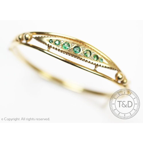 172 - An Edwardian style 9ct gold hinged bangle, set with seven graduated old cut emeralds interspersed wi... 