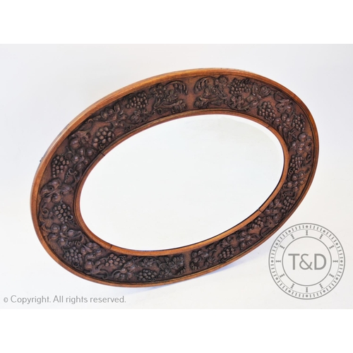 798 - An early 20th century carved oak oval wall mirror, the frame carved in relief with trailing grape vi... 