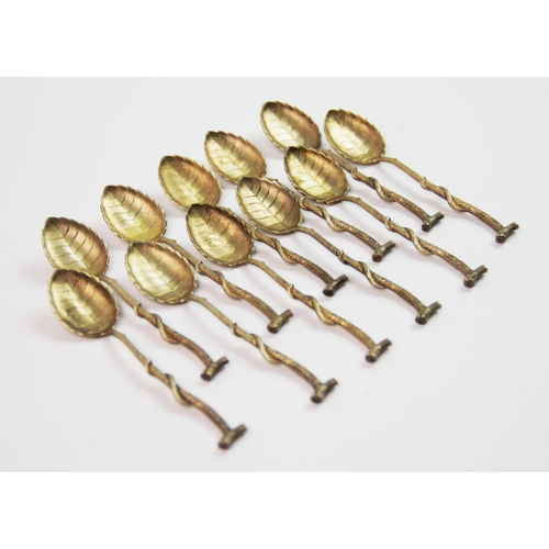 21 - A set of eleven continental silver gilt teaspoons, the bowls designed as leaves, the handles of twig... 