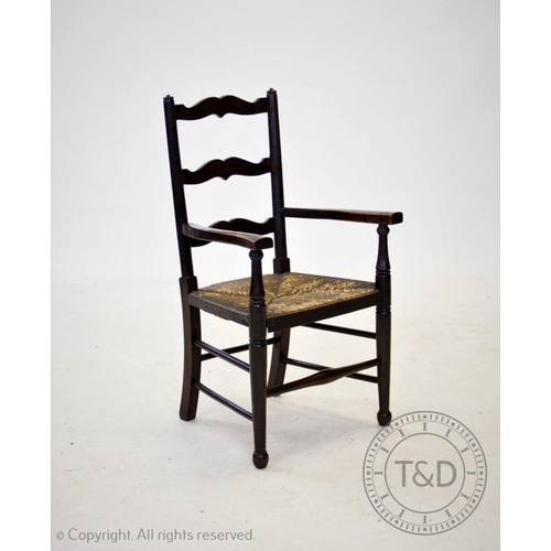 858 - An early 20th century child's rush seat beech elbow chair, with three rungs above an envelope rush s... 