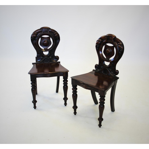 861 - A pair of Victorian mahogany hall chairs, with a carved scrolling openwork back, centred with a roun... 