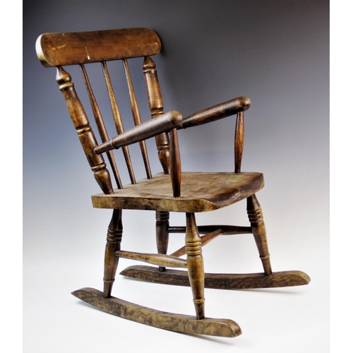 899 - A child's elm and beech wood spindle back rocking chair, with three tapering spindles above a shaped... 