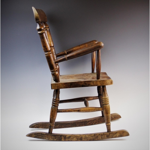 899 - A child's elm and beech wood spindle back rocking chair, with three tapering spindles above a shaped... 