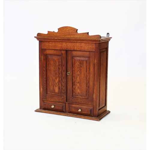 903 - An early 20th century oak wall cabinet, with a shaped pediment above a pair of panelled doors, enclo... 