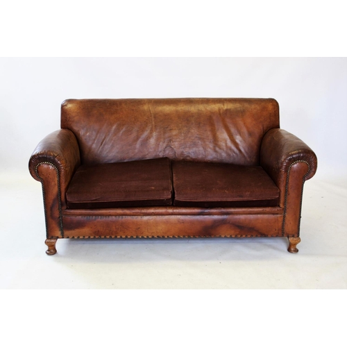 918 - An early 20th century tan leather three piece lounge suite, the two seater settee with padded scroll... 