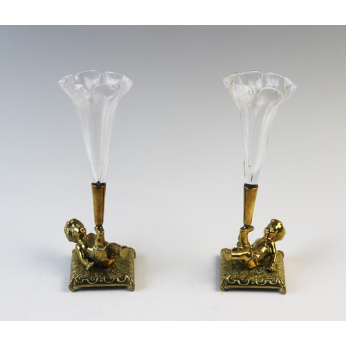 269 - A pair of brass cherub posy holders, each modelled as a tumbling child on a cushion supporting an as... 