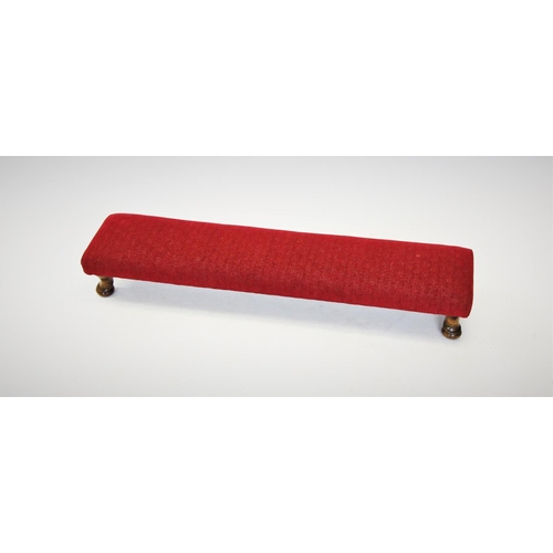 705 - A narrow footstool, mid 20th century, the red upholstered top raised upon stained beech wood squat c... 