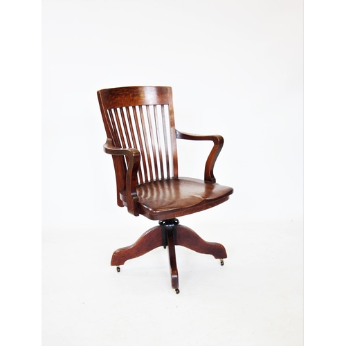 716 - A late 19th/early 20th century oak revolving office desk chair, with a rail back above a saddle shap... 