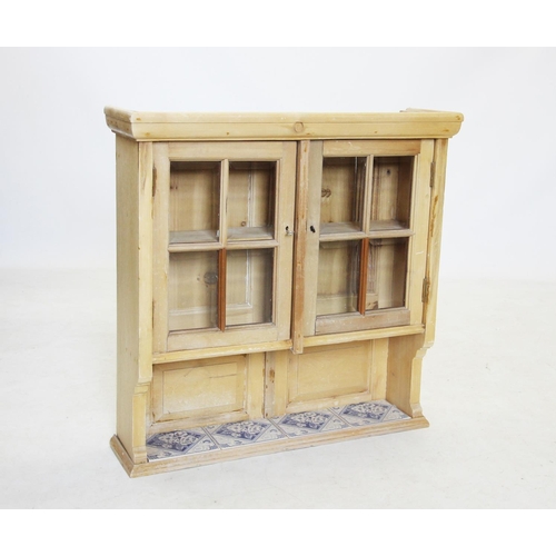 711 - A glazed pine wall cupboard, early 20th century, the glazed doors above a single shelf inset with fo... 