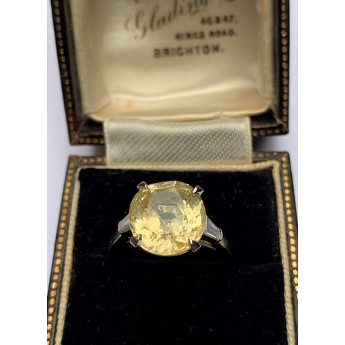 122 - A yellow sapphire and diamond ring, the central cushion mixed cut sapphire claw set with a baguette ... 