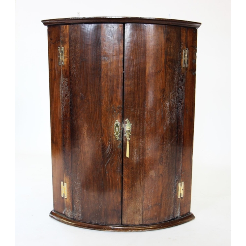 831 - A George III oak bow front hanging corner cupboard, the pair of doors on 'H' brass hinges, enclosing... 