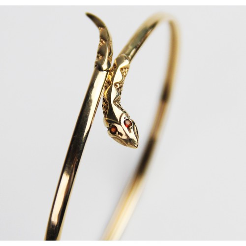 269 - A 9ct gold snake bangle, the plain polished oval bangle with stylised snake head and tail, with two ... 