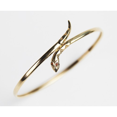 269 - A 9ct gold snake bangle, the plain polished oval bangle with stylised snake head and tail, with two ... 