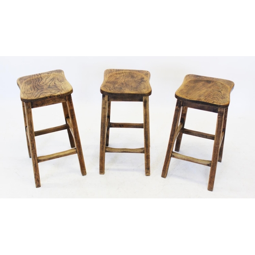 1047 - A trio of mid 20th century elm seated stools, the shaped and figured elm seats raised upon out set l... 