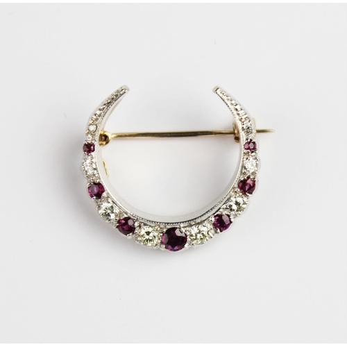 200 - A diamond and ruby set crescent brooch, comprising eight graduated round brilliant cut diamonds and ... 