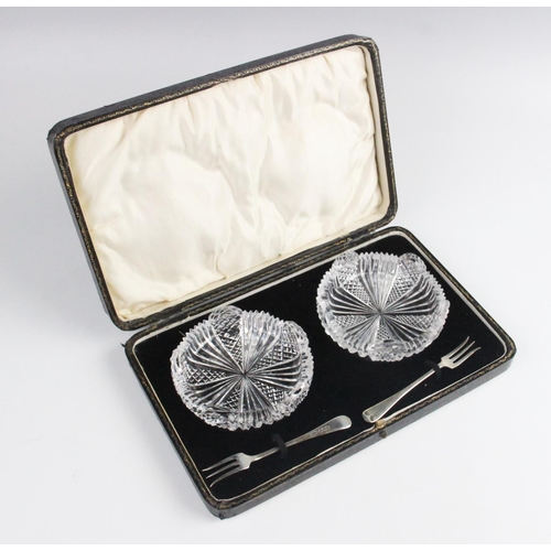 96 - A cased pair of cut glass butter dishes, each 8.7cm wide, each with accompanying silver butter knive... 