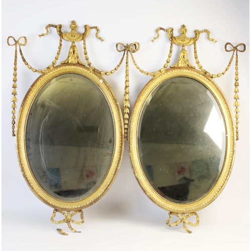 1023 - A pair of 19th century gilt wood and gesso oval wall mirrors, each with an Adams style, urn shaped c... 