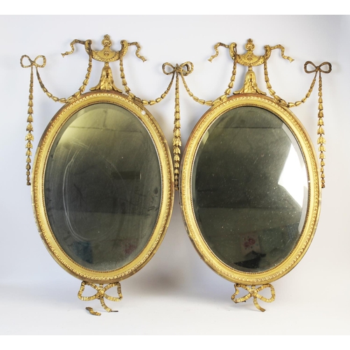 1023 - A pair of 19th century gilt wood and gesso oval wall mirrors, each with an Adams style, urn shaped c... 