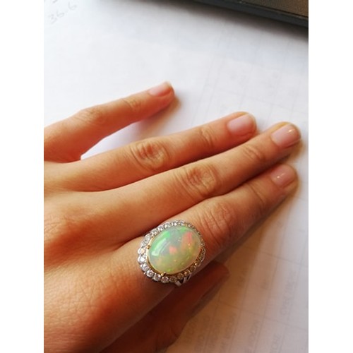 192 - An opal and diamond cluster ring, the central oval natural opal cabochon (measuring 15.2mm x 11.4mm)... 