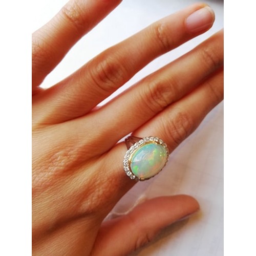 192 - An opal and diamond cluster ring, the central oval natural opal cabochon (measuring 15.2mm x 11.4mm)... 