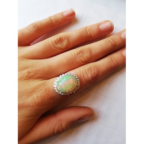 192 - An opal and diamond cluster ring, the central oval natural opal cabochon (measuring 15.2mm x 11.4mm)... 