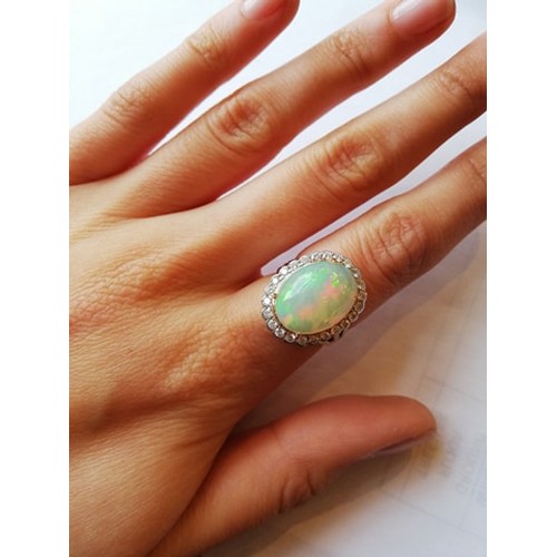 192 - An opal and diamond cluster ring, the central oval natural opal cabochon (measuring 15.2mm x 11.4mm)... 