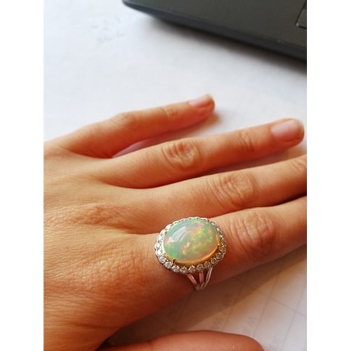 192 - An opal and diamond cluster ring, the central oval natural opal cabochon (measuring 15.2mm x 11.4mm)... 