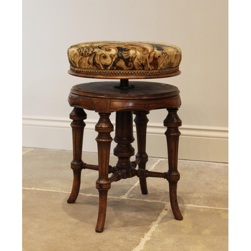 563 - A late Victorian walnut revolving piano stool, the circular padded seat above a shaped apron, raised... 