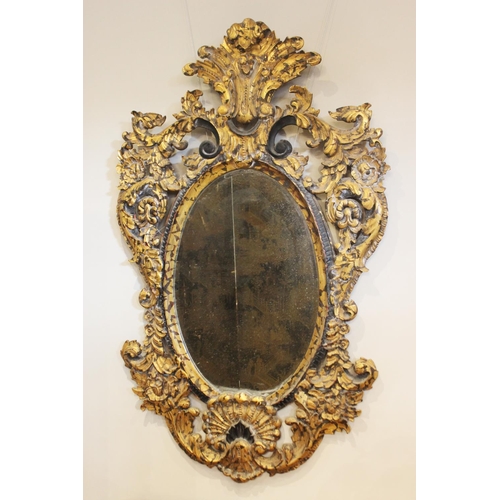 600 - A French Rococo style parcel gilt wall mirror, the bevelled oval mirror plate within an elaborately ... 