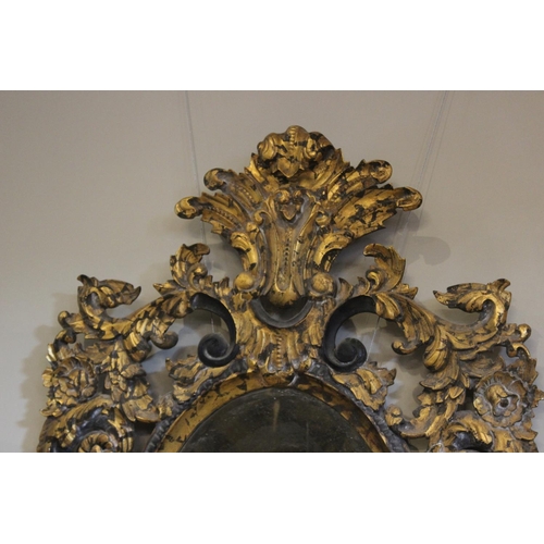 600 - A French Rococo style parcel gilt wall mirror, the bevelled oval mirror plate within an elaborately ... 