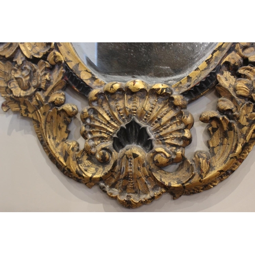 600 - A French Rococo style parcel gilt wall mirror, the bevelled oval mirror plate within an elaborately ... 