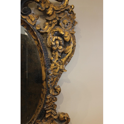 600 - A French Rococo style parcel gilt wall mirror, the bevelled oval mirror plate within an elaborately ... 