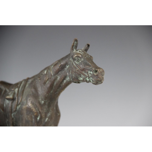 340 - A bronze patinated sculpture of a racehorse, modelled standing saddled, set to a green marble plinth... 