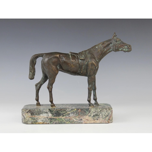 340 - A bronze patinated sculpture of a racehorse, modelled standing saddled, set to a green marble plinth... 