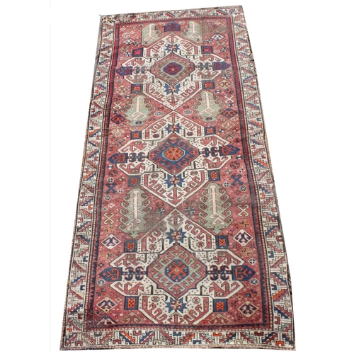 388 - A large Turkish wool runner, with three geometric medallions upon a red ground, within a conforming ... 