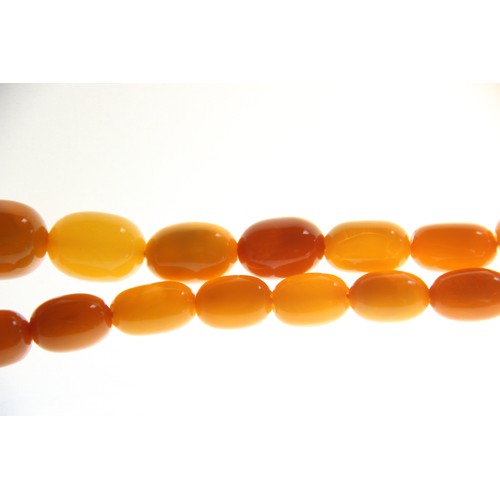 99 - A butterscotch amber bead necklace, comprising fifty-one graduated plain polished oval beads measuri... 