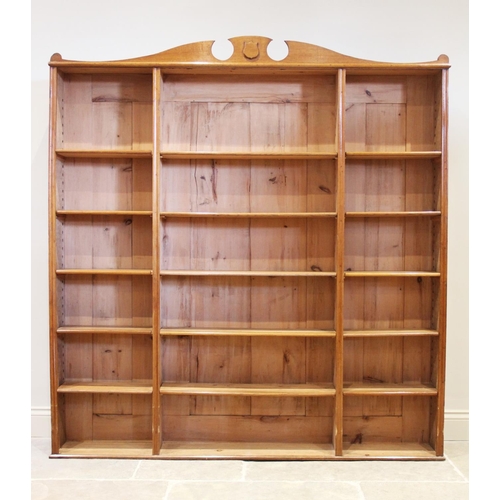 867 - An early 20th century honey oak open bookcase, the shaped pediment with a shield shaped motif above ... 