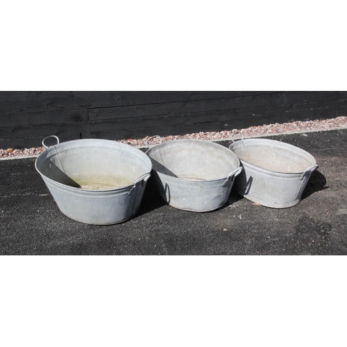 879 - Three graduated galvanised tubs, each of oval form, applied with side loop handles, the widest 86cm