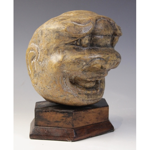 102 - A carved stone sculpture of a grinning grotesque mask, 15.5cm high, mounted upon a rod and hexagonal... 