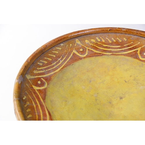 289 - A terracotta slipware footed dish, of circular form with three blade feet to base, the raised rim ab... 