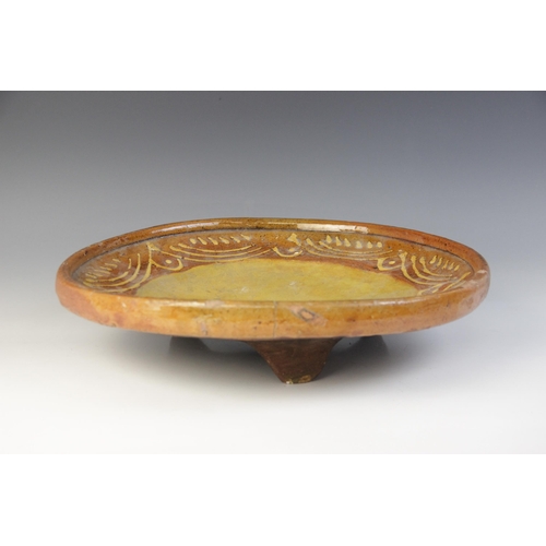 289 - A terracotta slipware footed dish, of circular form with three blade feet to base, the raised rim ab... 