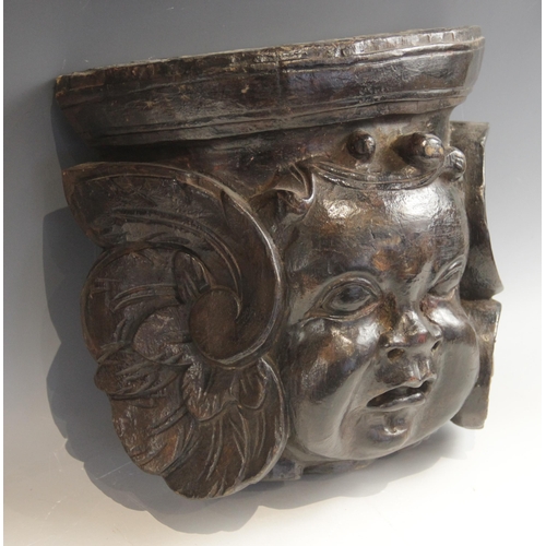 444 - A baroque carved corbel, designed with a cherub mask, flanked by scrolls, 30cm high x 32.5cm wide