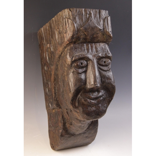 467 - An early 16th century naïve carved oak figural corbel, carved with a smiling face, within a scroll c... 